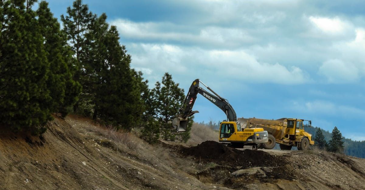 A yellow excavator is digging a hole in a dirt field