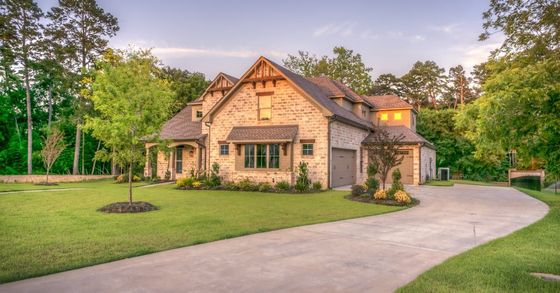 A large house with a driveway leading to it is surrounded by trees.