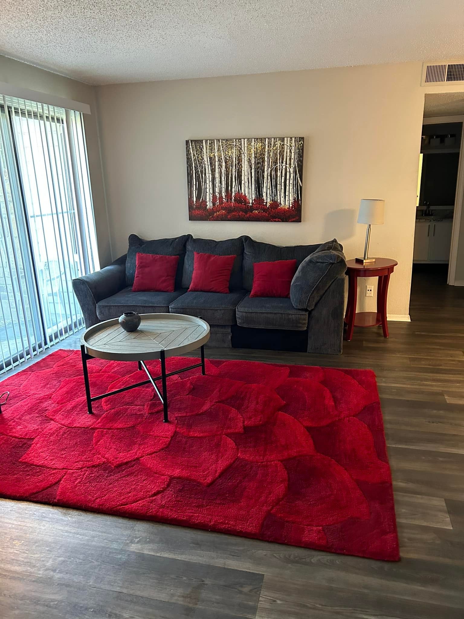 Living room with red rug, gray couch with red pillows, and tree artwork.