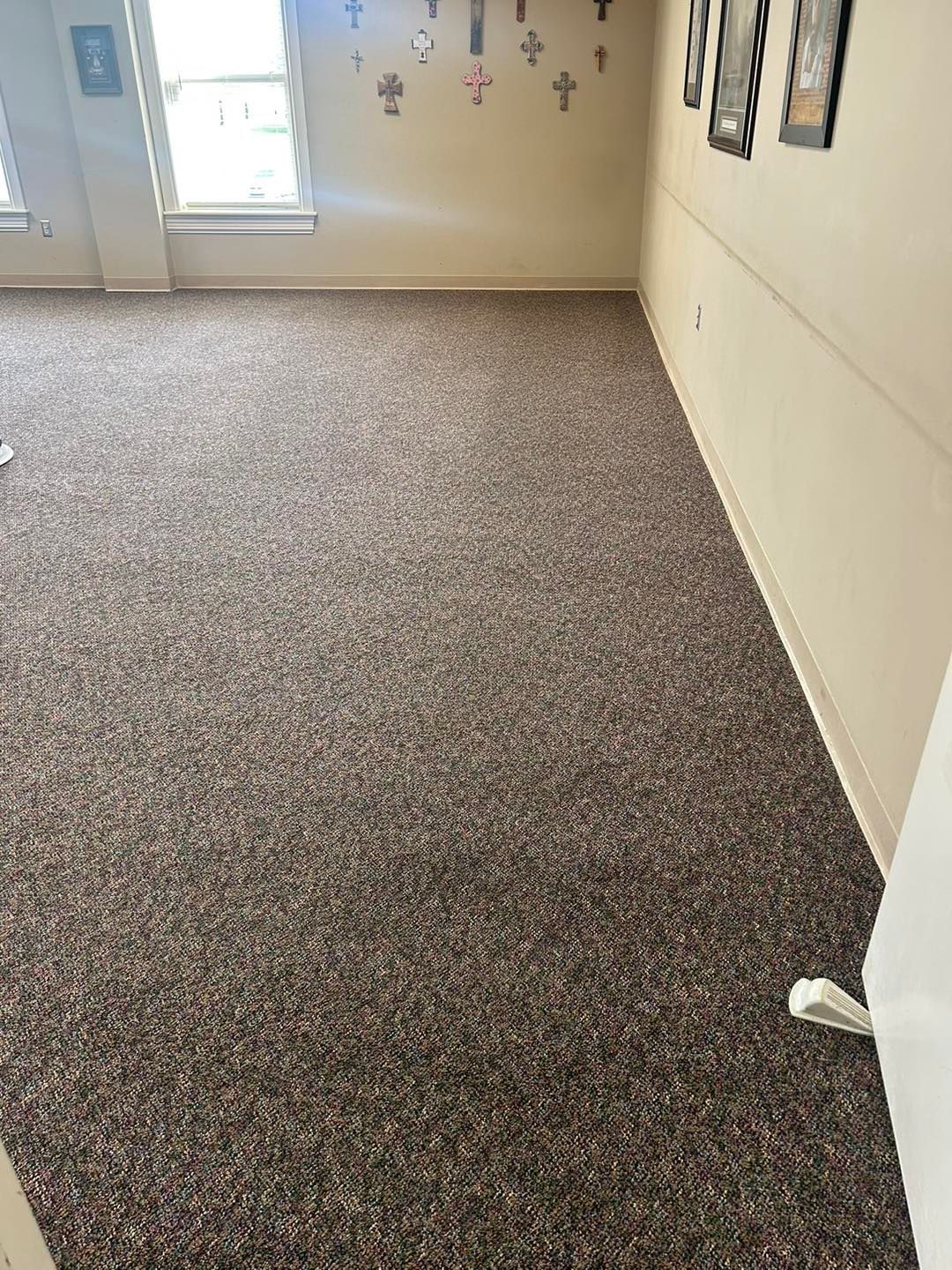 Brown speckled carpet in a room with light-colored walls, a window, and framed art.