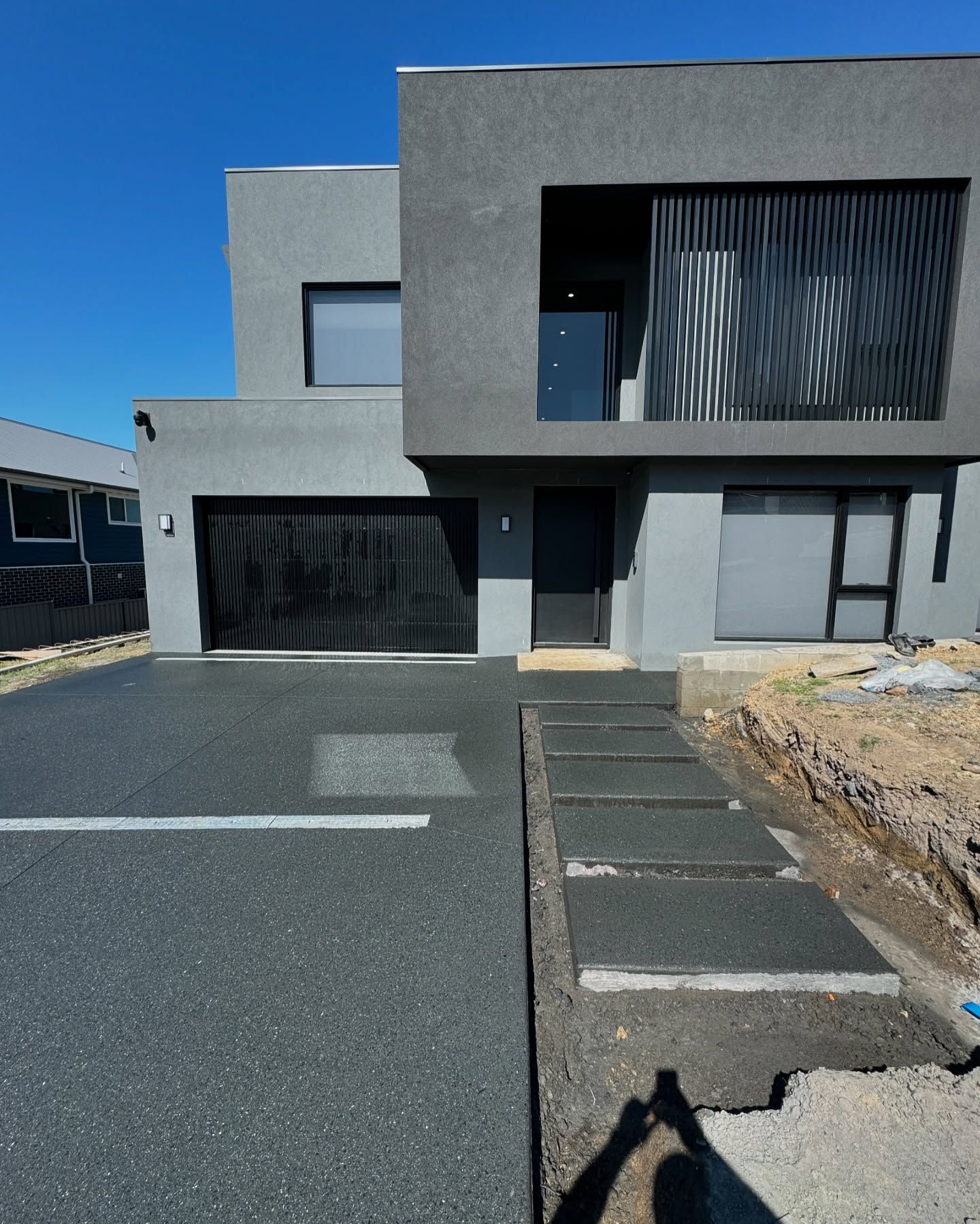 A Two-story, Modern Grey House With a Dark Garage Door — JDB Concreting in Horsley, NSW
