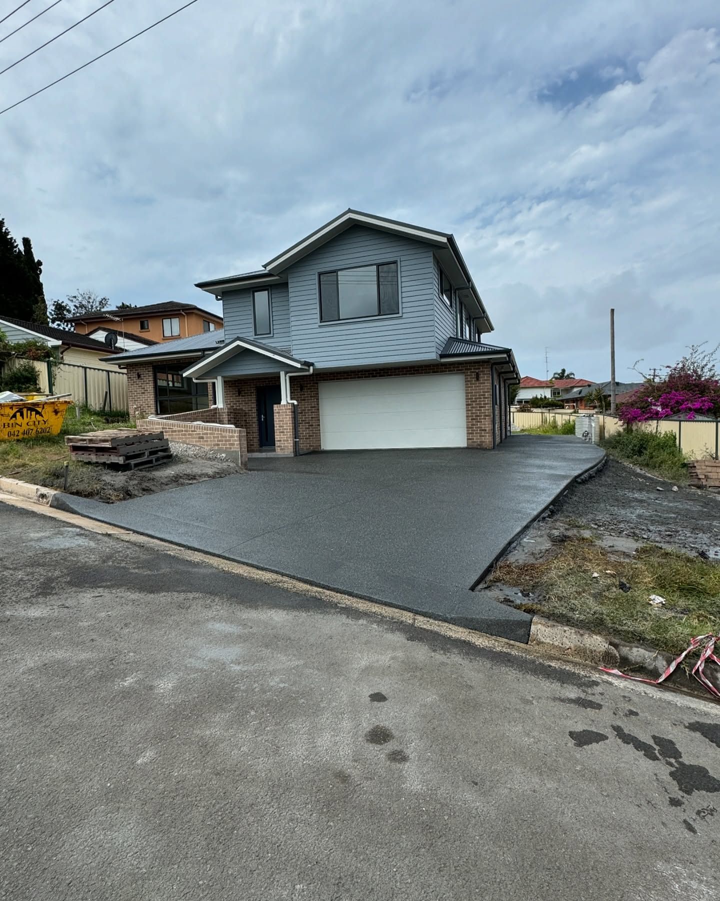 A Two-story Blue House and a Freshly Paved Dark Asphalt Driveway — JDB Concreting in Southern Highlands, NSW