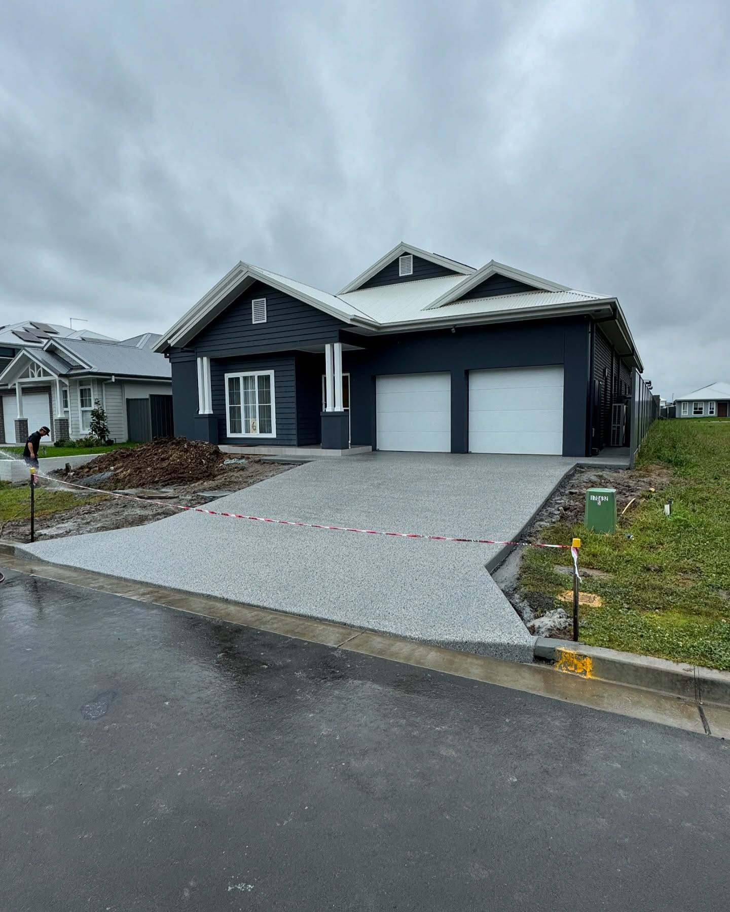 A modern navy blue house with a white roof and garage doors features a freshly laid, speckled grey driveway. — JDB Concreting in Horsley, NSW