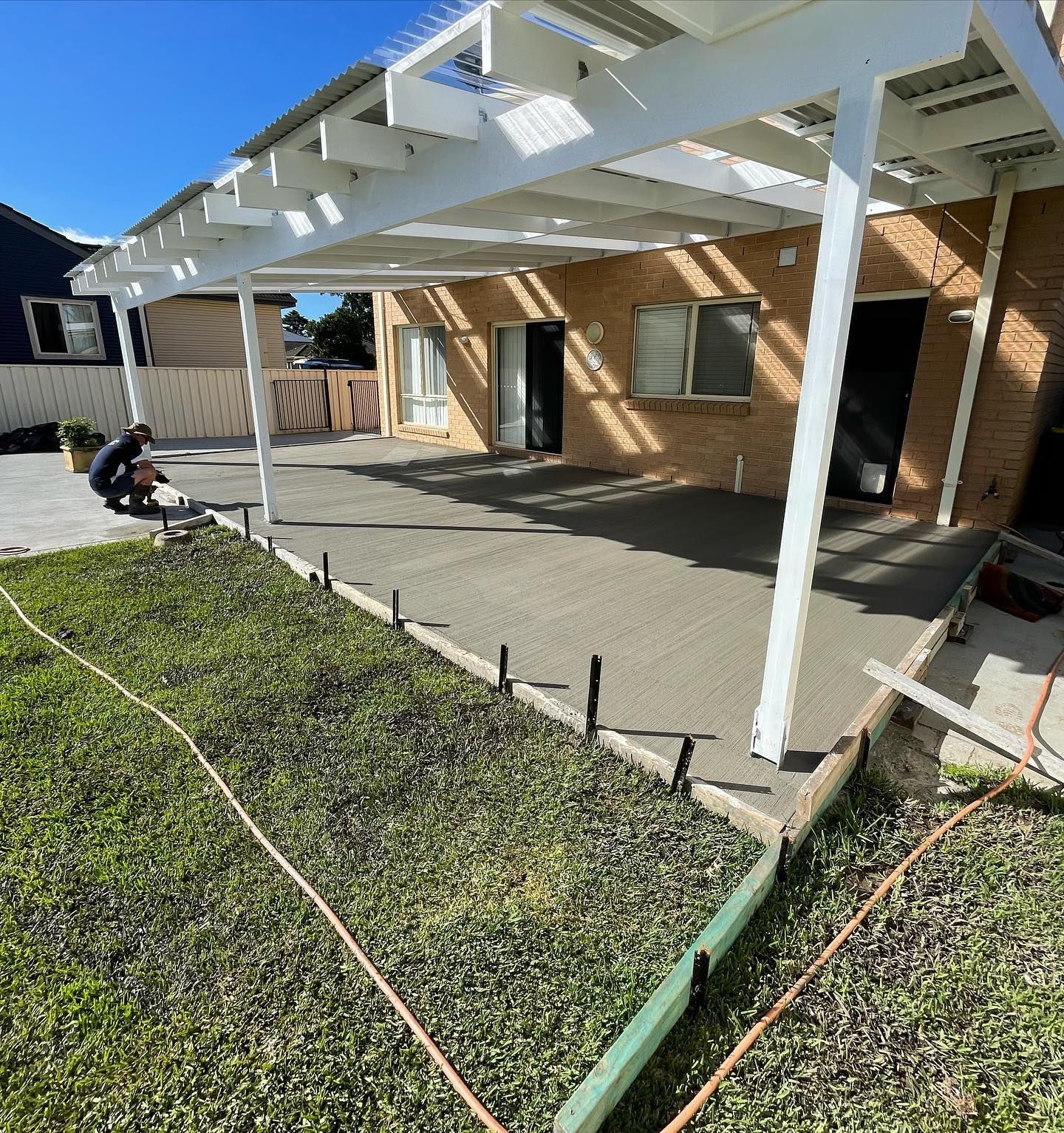 A Person Finishes Pouring a Concrete Patio Under a White Pergola — JDB Concreting in Horsley, NSW
