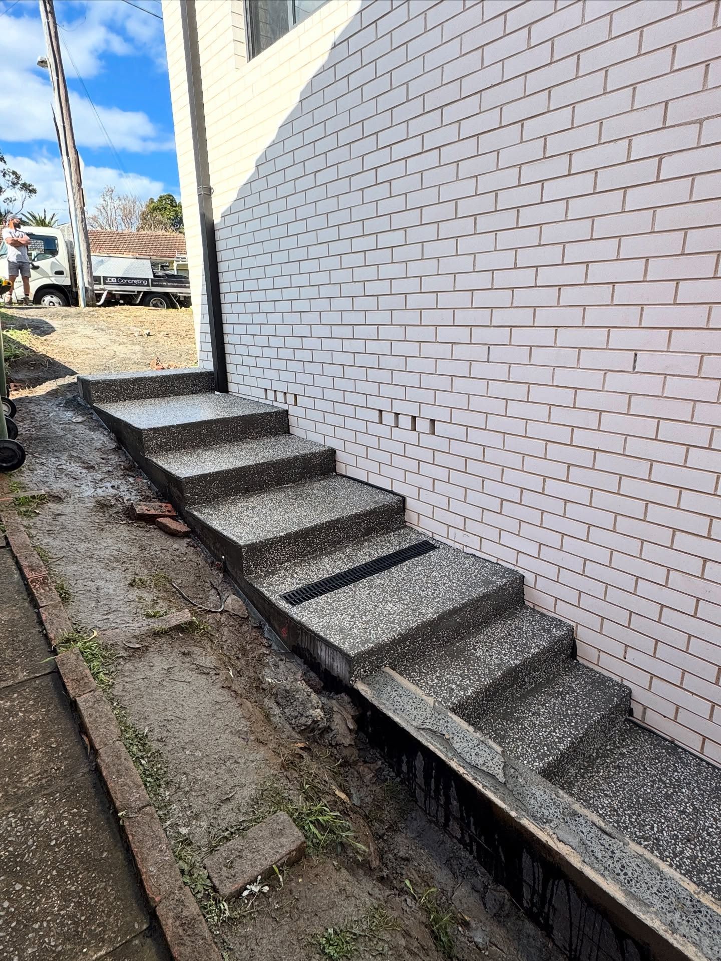 Concrete Steps With an Exposed Aggregate Finish Run Alongside a White Brick Wall — JDB Concreting in Horsley, NSW