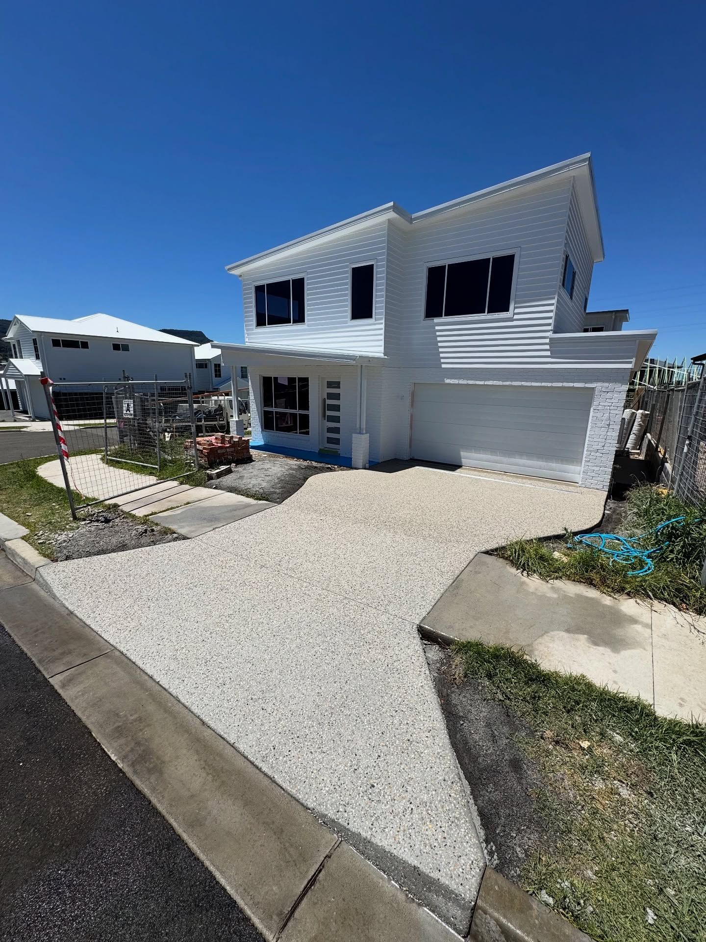 A two-story white house with a modern slanted roof and a large, textured stone driveway under a clear blue sky. — JDB Concreting in Horsley, NSW