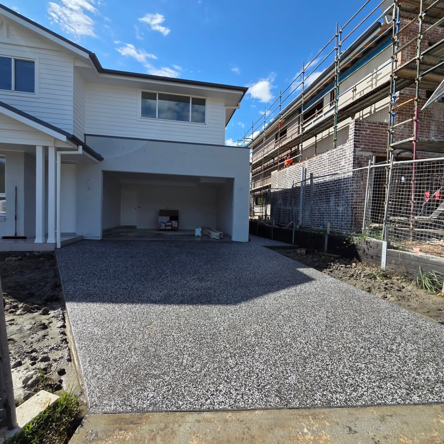A modern house with a white exterior, a grey garage, and a newly laid dark exposed aggregate concrete driveway. — JDB Concreting in Horsley, NSW
