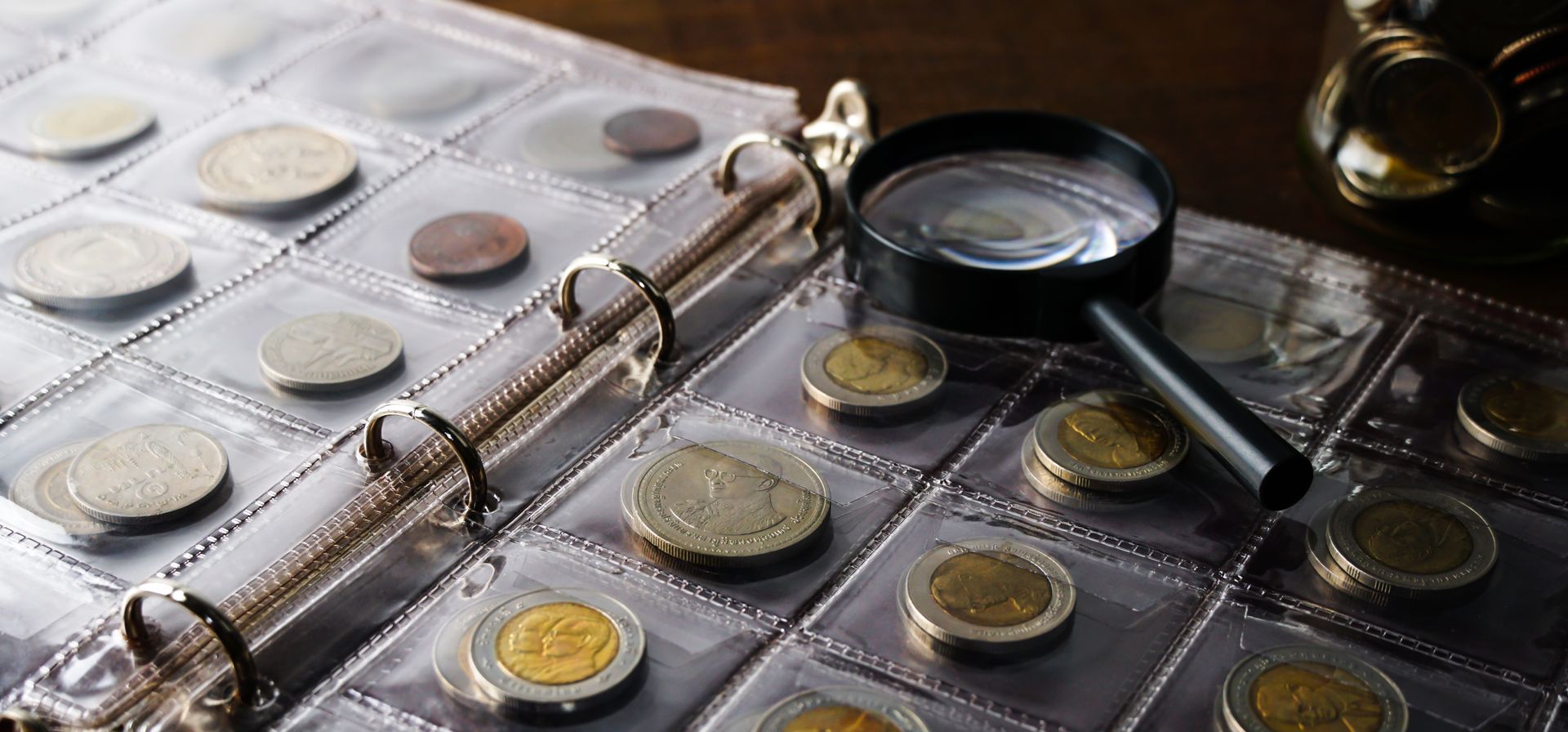 Coin collection in a binder with a magnifying glass placed on top of plastic sleeves.