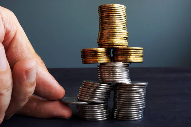 Stacks of gold and silver coins arranged in a structure with a hand adding a coin for financial growth.