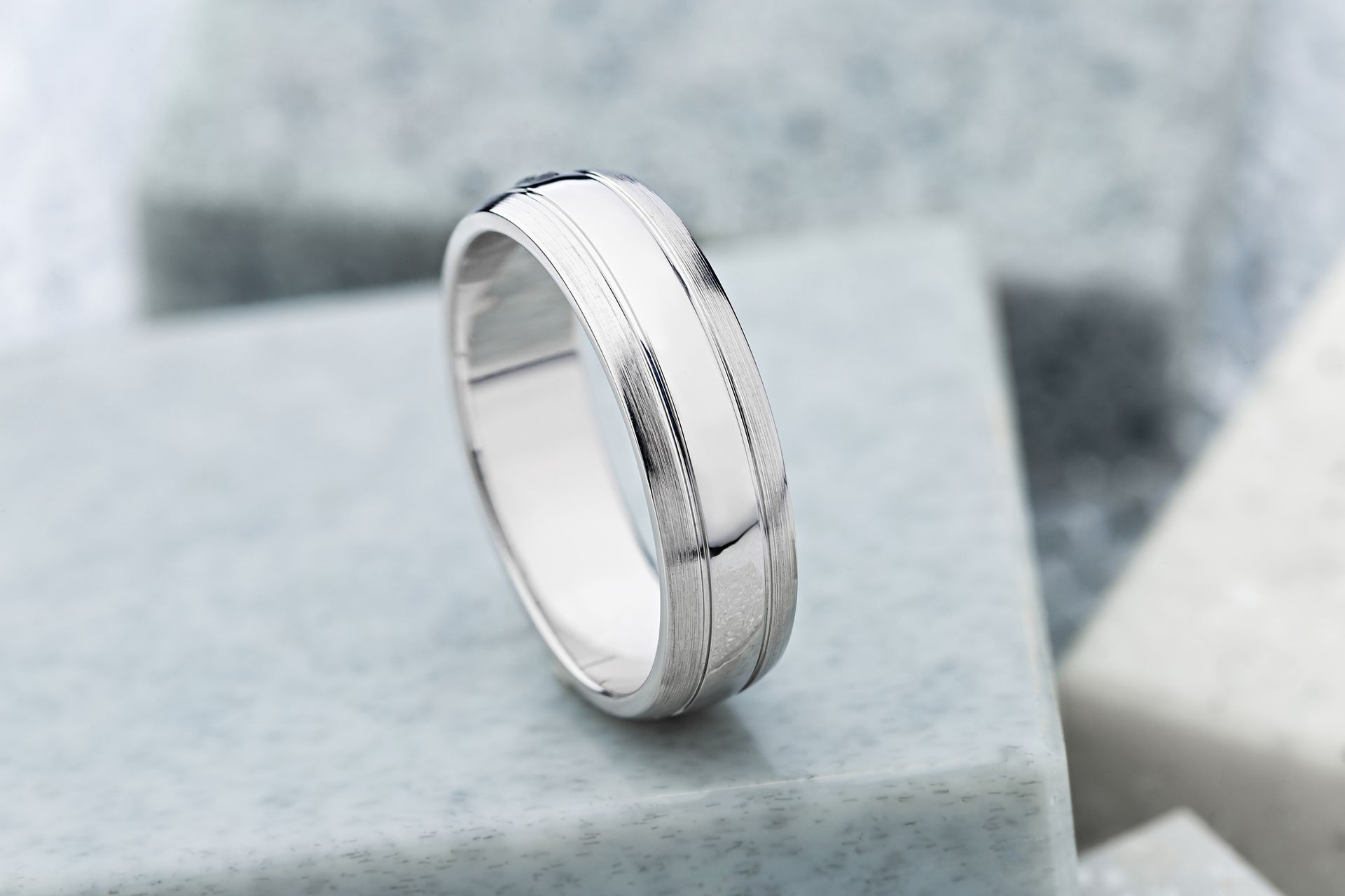 A white gold ring is sitting on top of a marble block.