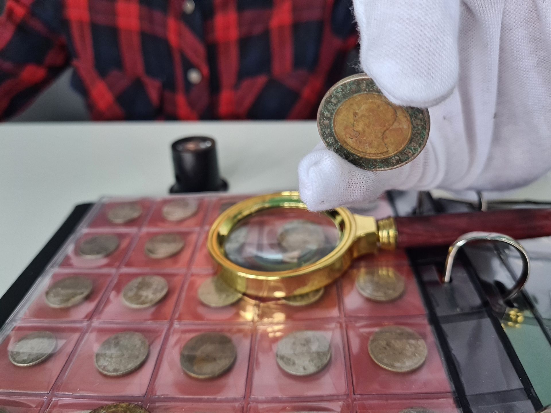 A person is holding a coin in front of a magnifying glass.