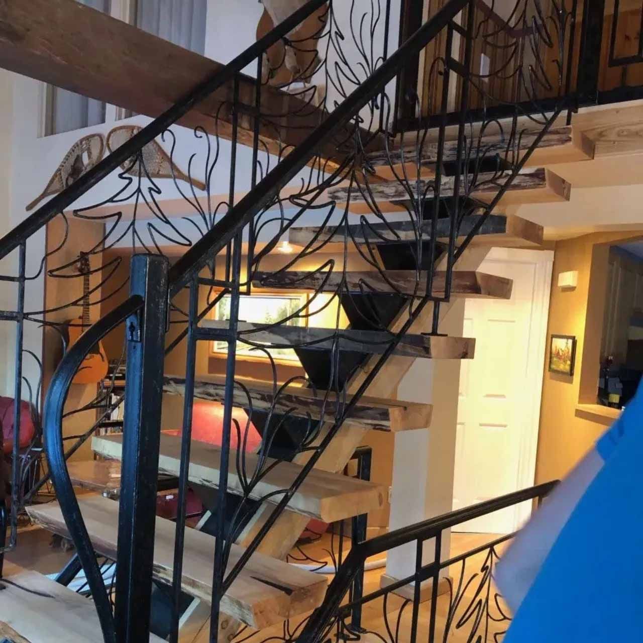 Un escalier avec des marches en bois naturel et des rampes en métal noir ornées de motifs d'arbres en fer forgé.