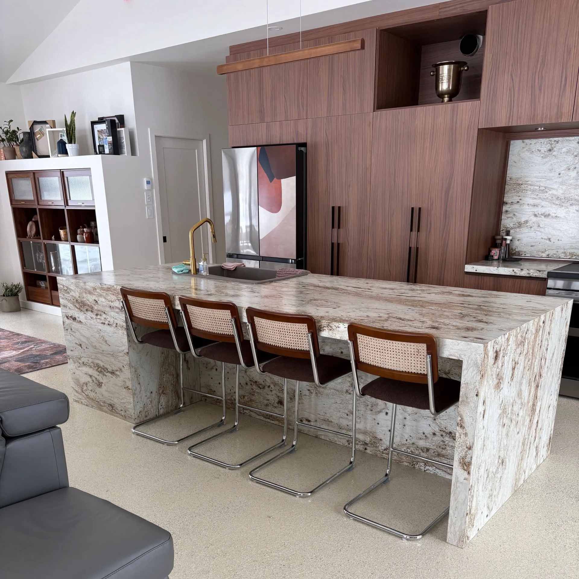 Cuisine moderne avec un grand îlot central en marbre à effet cascade, quatre chaises à dossier en rotin et des armoires en bois.