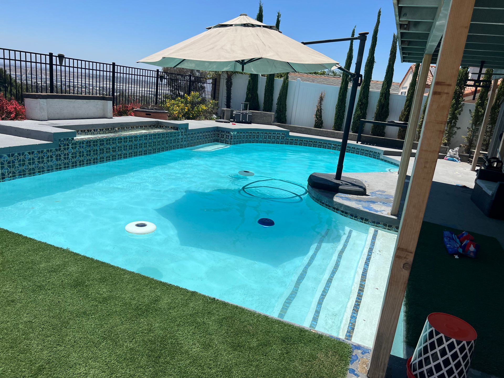 A swimming pool with turquoise water, patio umbrella, and artificial grass.