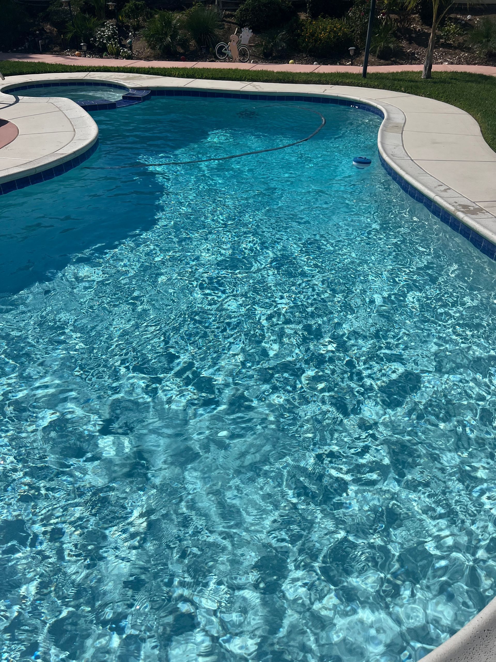 Blue swimming pool with rippling water, concrete border, and green grass in the background.