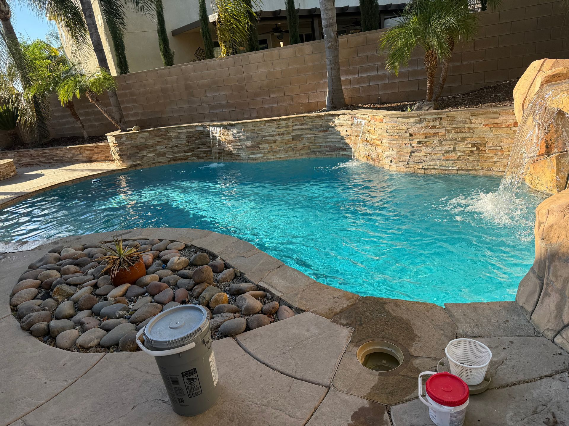 A swimming pool with a waterfall in the background and buckets of water on the side of it.