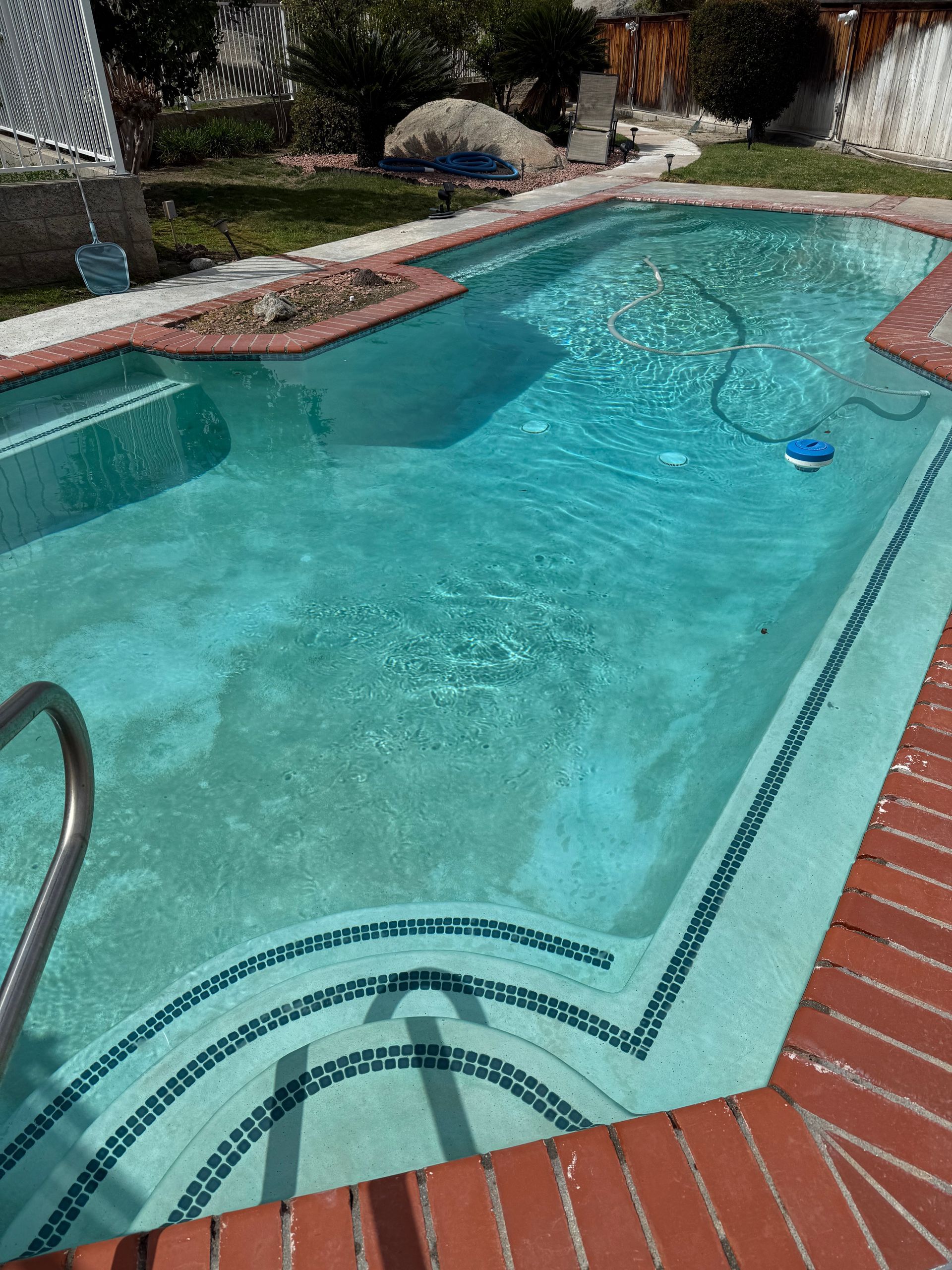 Swimming pool with blue water, brick coping, and steps.