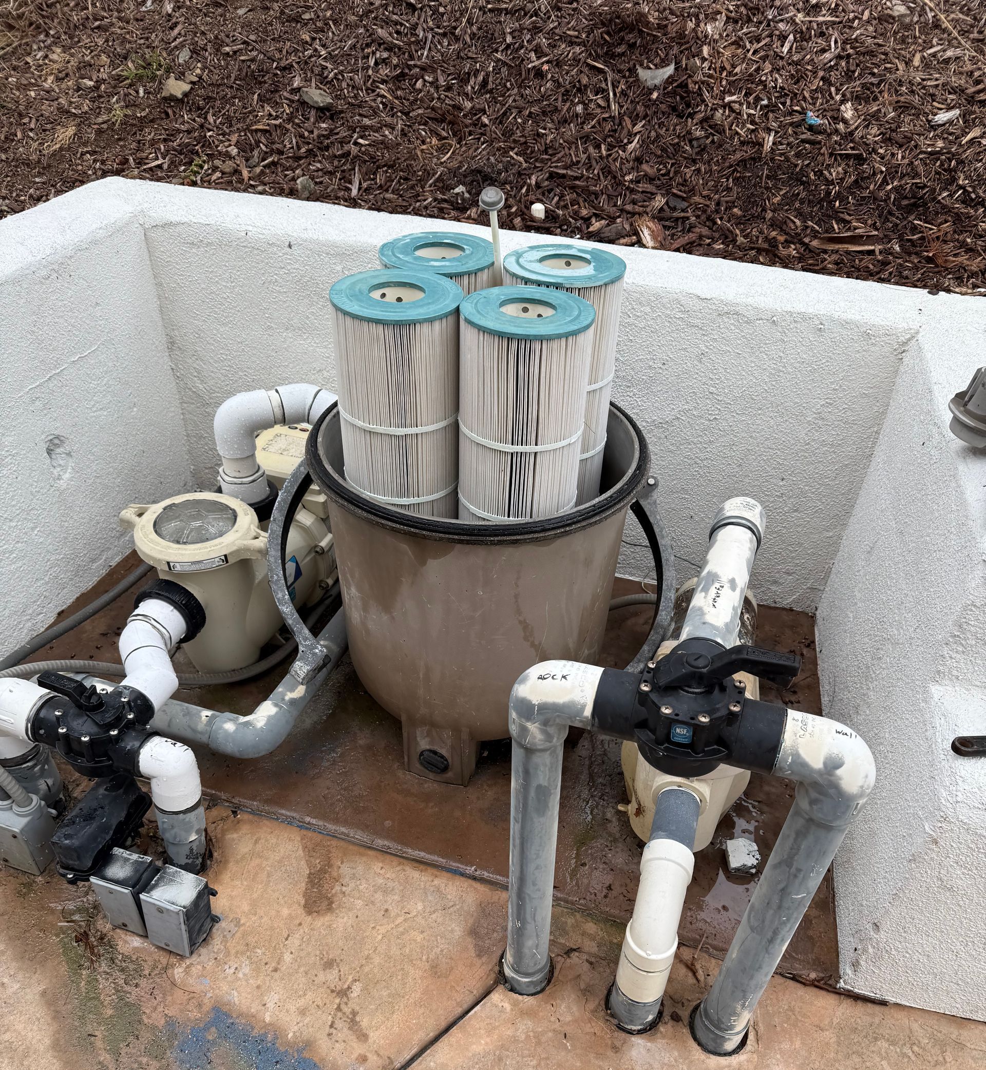 A bucket filled with filter cartridges is sitting next to a pool pump.