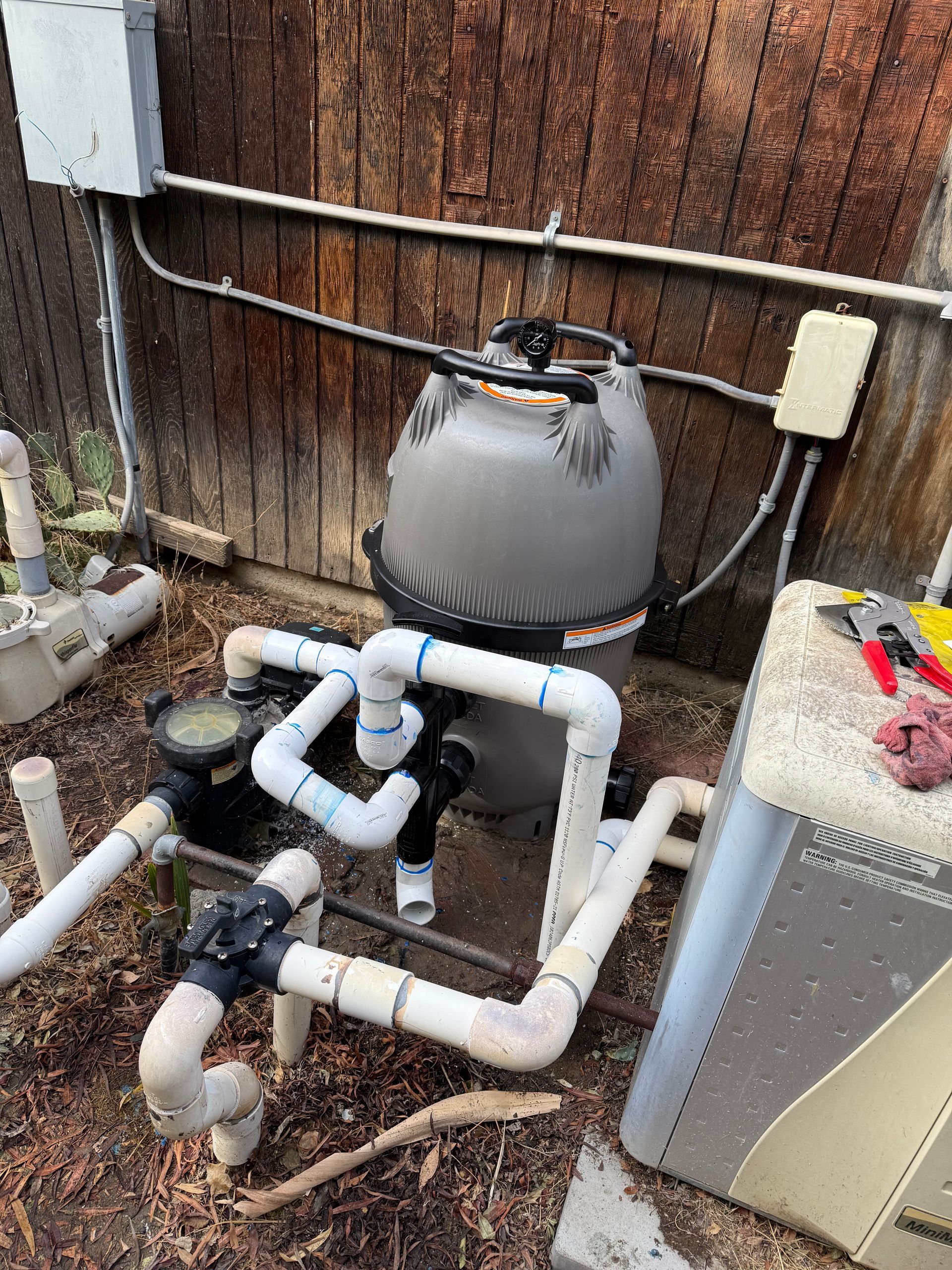 A swimming pool filter is sitting on the ground next to a wooden fence.