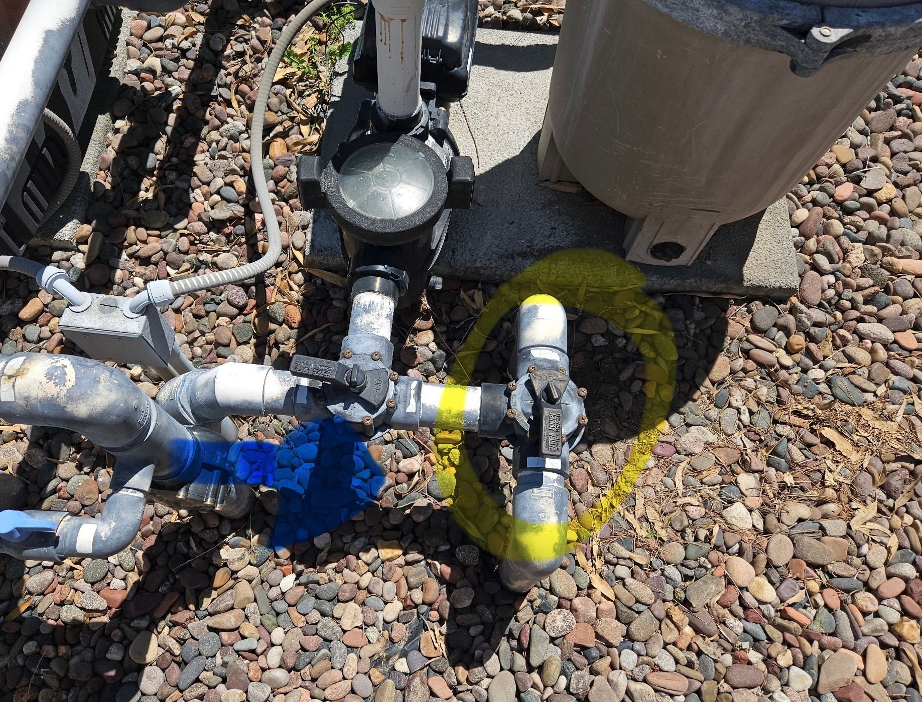 Close-up of pool equipment with a valve highlighted in yellow against a background of gravel.