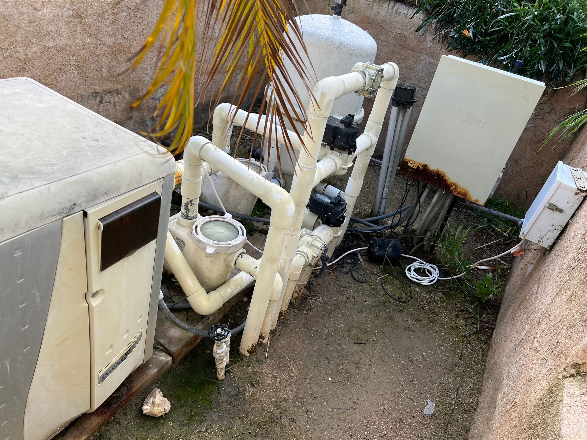 Pool equipment, pipes and machinery against a wall in an outdoor setting.