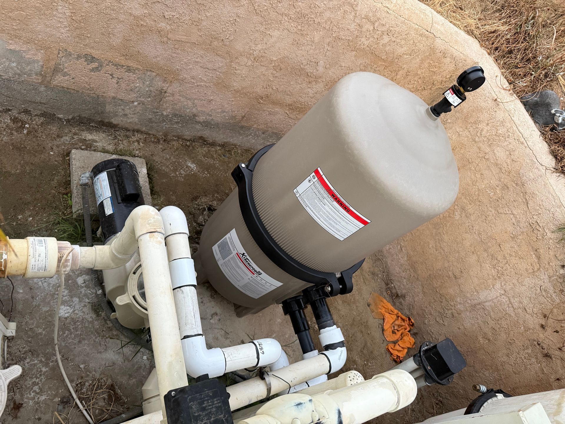 Pool plumbing with a beige filter tank and white PVC pipes in a concrete pit