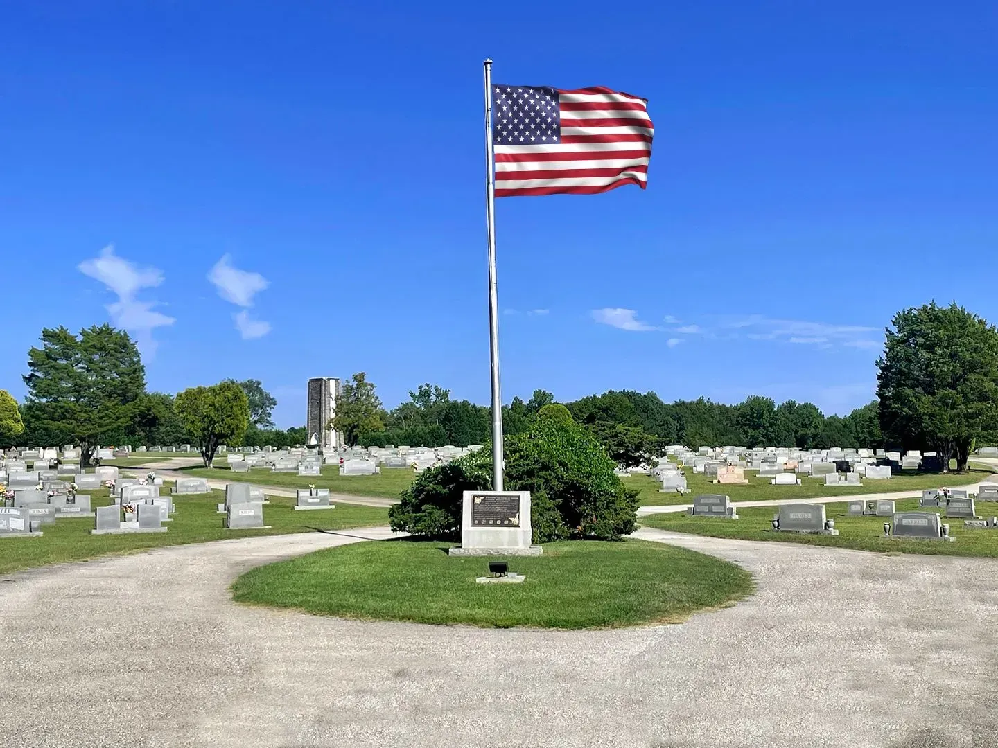 American flag on a pole in a cemetery with rows of headstones and a curved gravel path