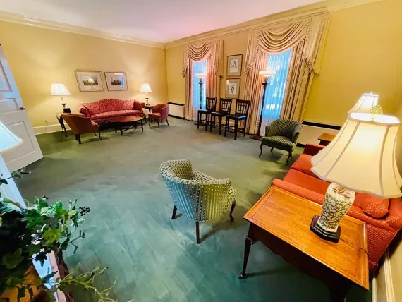 Elegant living room with yellow walls, orange sofas, green carpet, and tall curtained windows