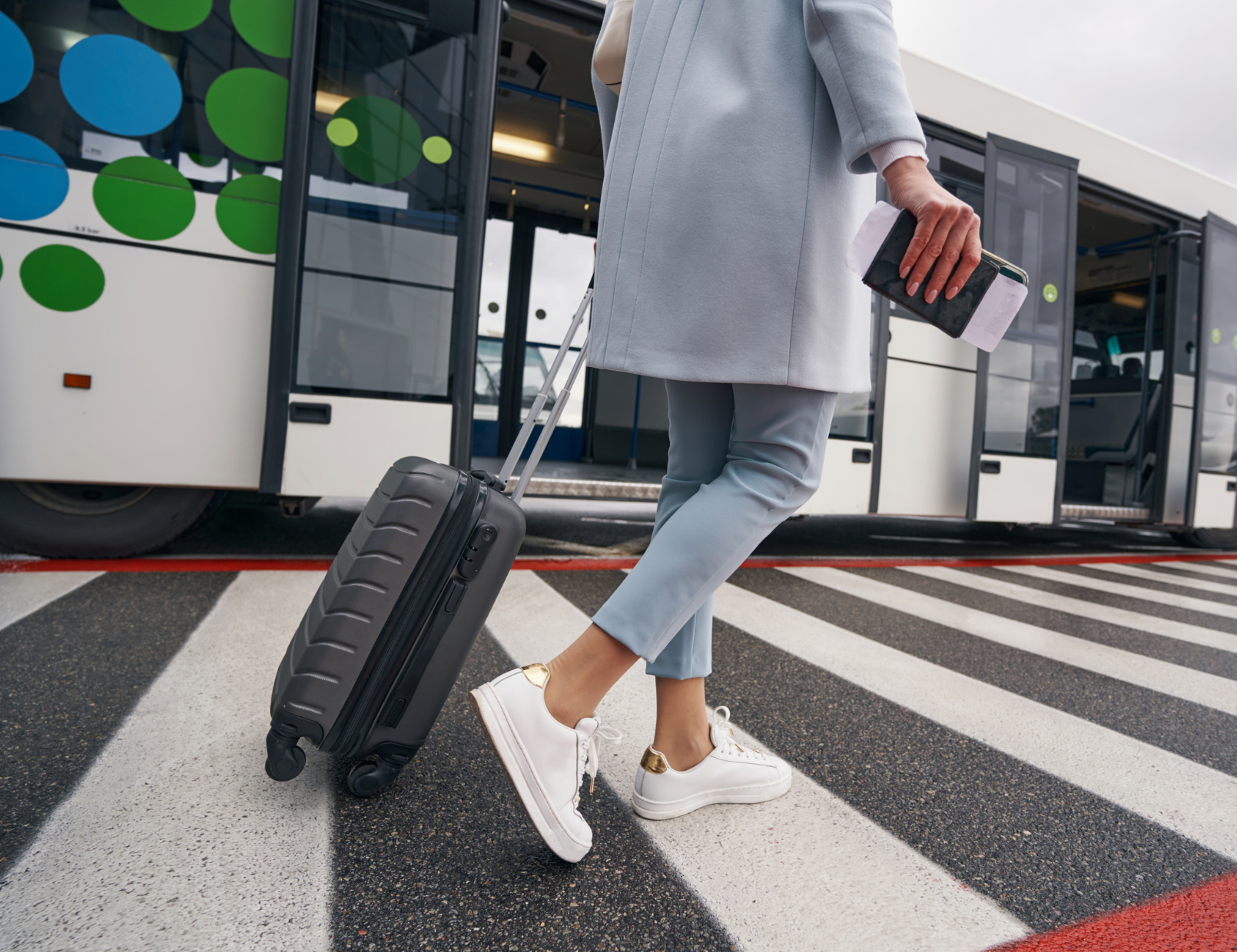 A woman is walking with a suitcase and a passport in front of a bus.