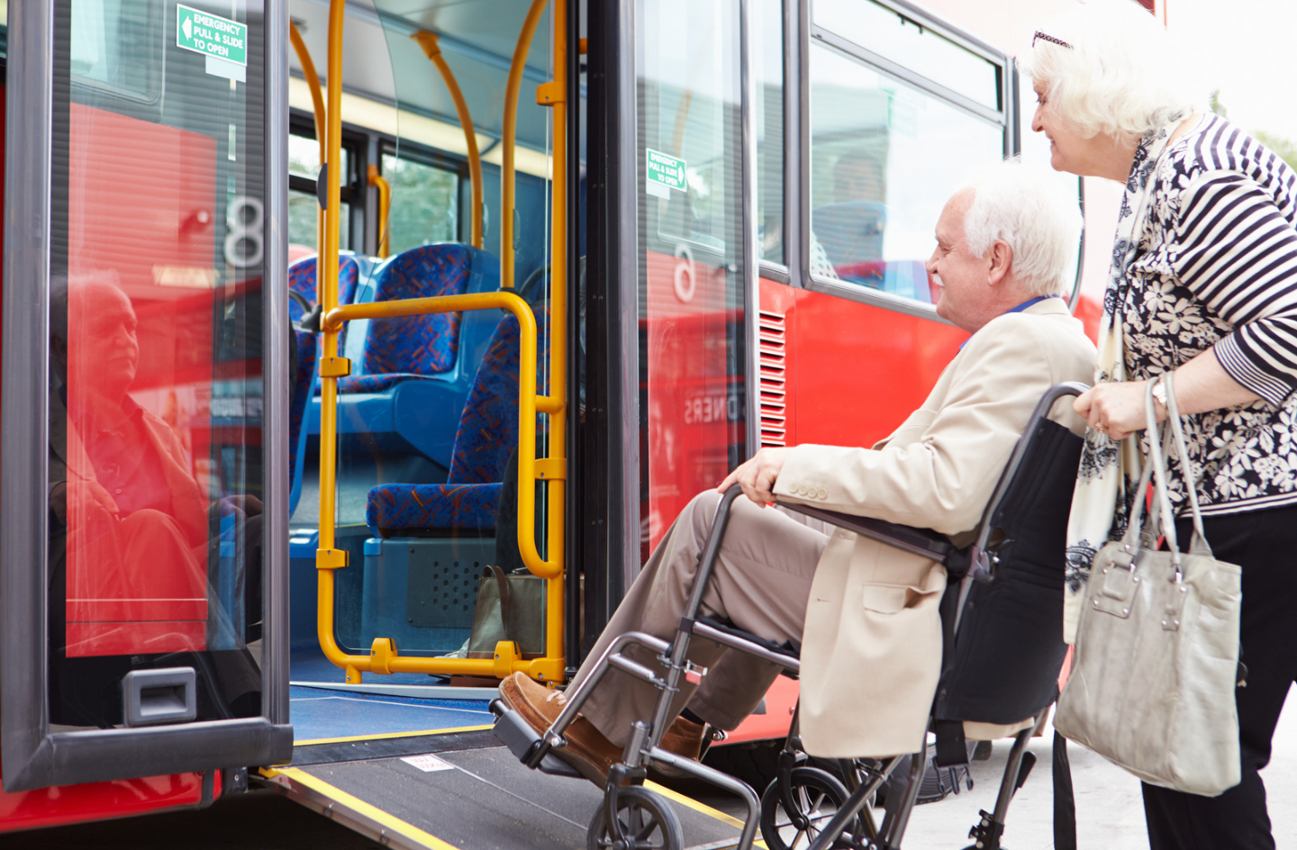 An elderly man in a wheelchair is getting on a bus.