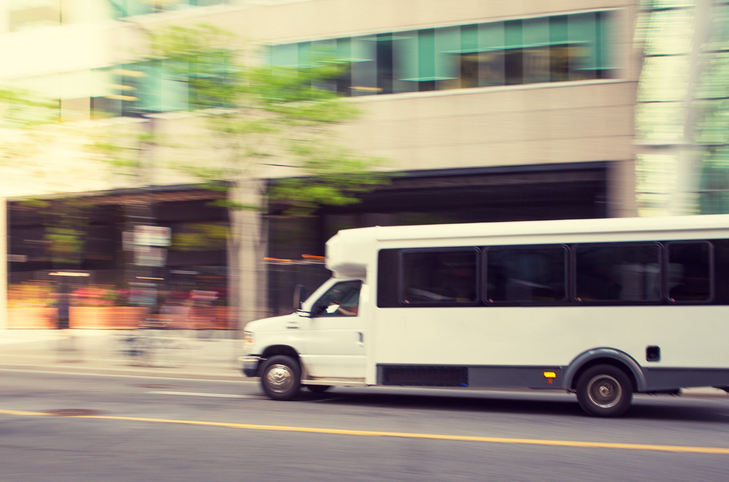 A white bus is driving down the street in front of a building.