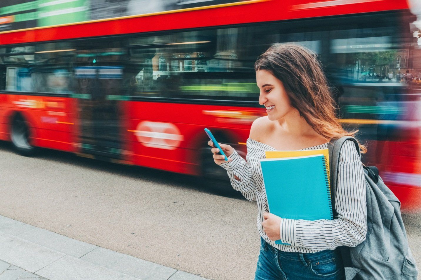 A woman is standing in front of a double decker bus looking at her phone.