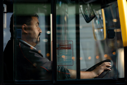 A man is driving a bus at night and looking out the window.