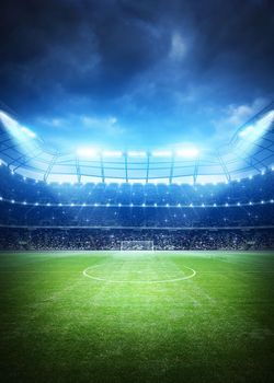 Un estadio de fútbol brillantemente iluminado por la noche, con un campo verde y una portería a lo lejos bajo un cielo nublado y dramático.