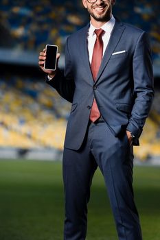 Un profesional vestido de traje sonríe mientras sostiene un teléfono inteligente en un estadio grande y vacío.