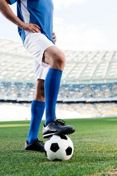Un jugador de fútbol con uniforme azul y blanco está de pie en un campo con un pie apoyado sobre un balón de fútbol.
