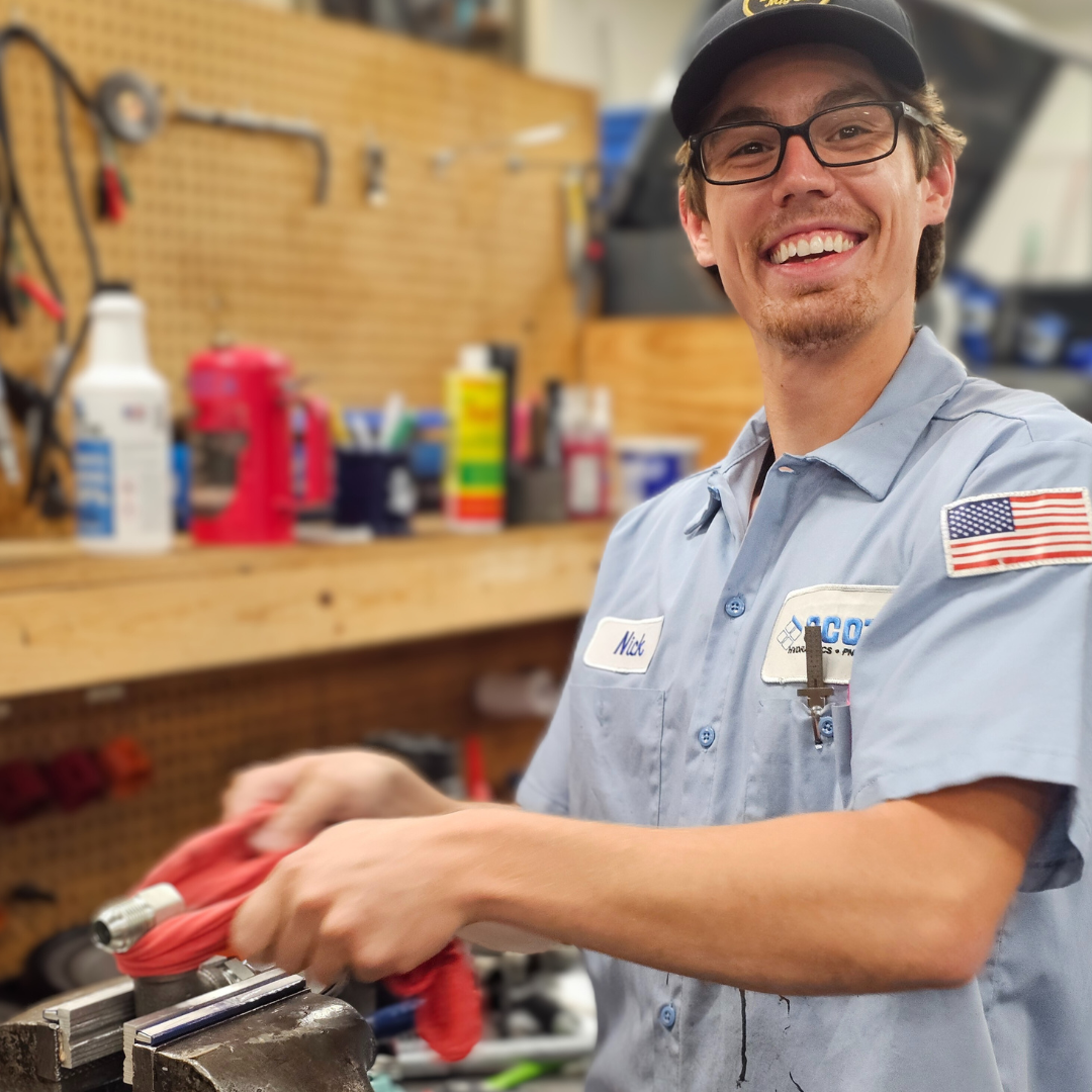 A man wearing glasses and a hat is working on a vise