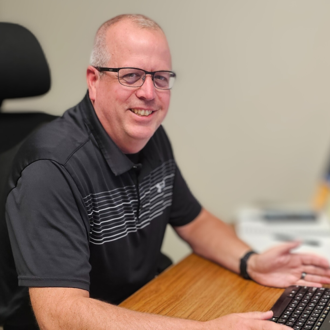 A man wearing glasses is sitting at a desk with a laptop