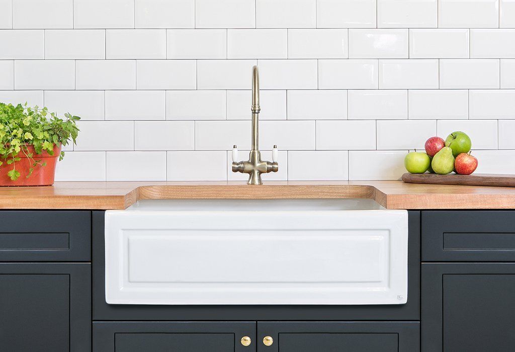 A farmhouse sink against timber bench top, navy cabinets and white subway tile.
