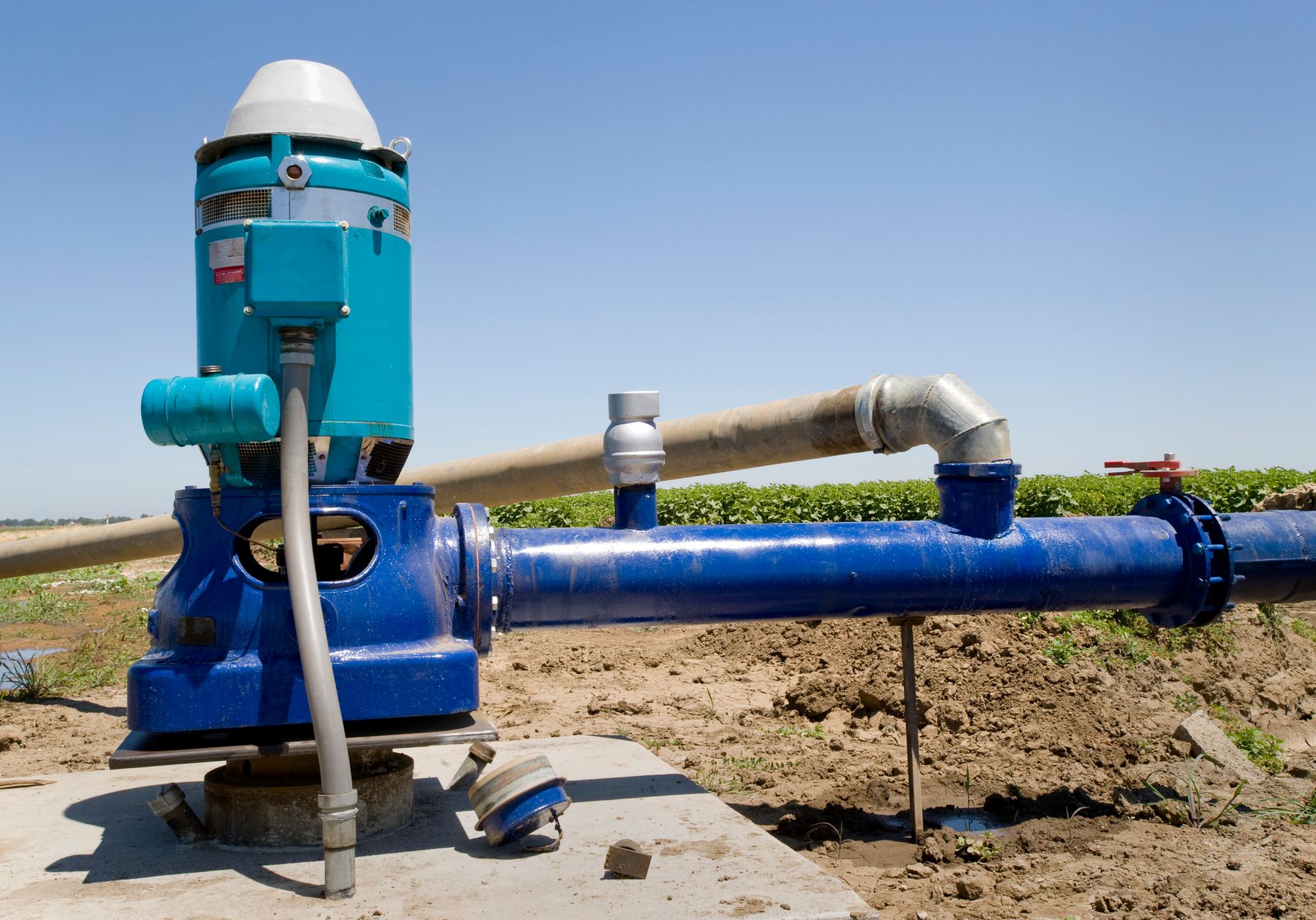 A blue water pump is sitting in the middle of a field.