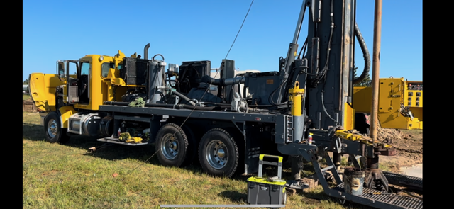 A woman wearing a mask and gloves is holding a test tube and a clipboard.