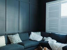 Navy blue sectional sofa against a dark blue paneled wall, with white shutters.