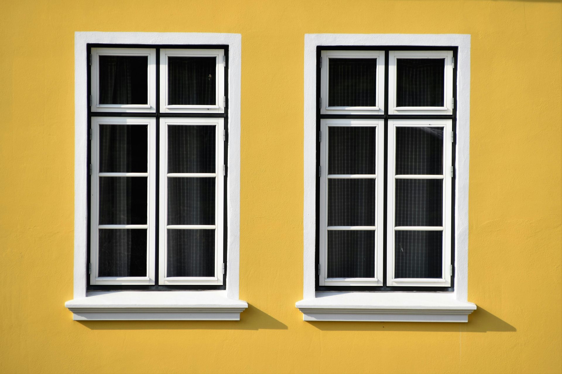 Two white-framed windows with black grid lines, on a yellow wall.
