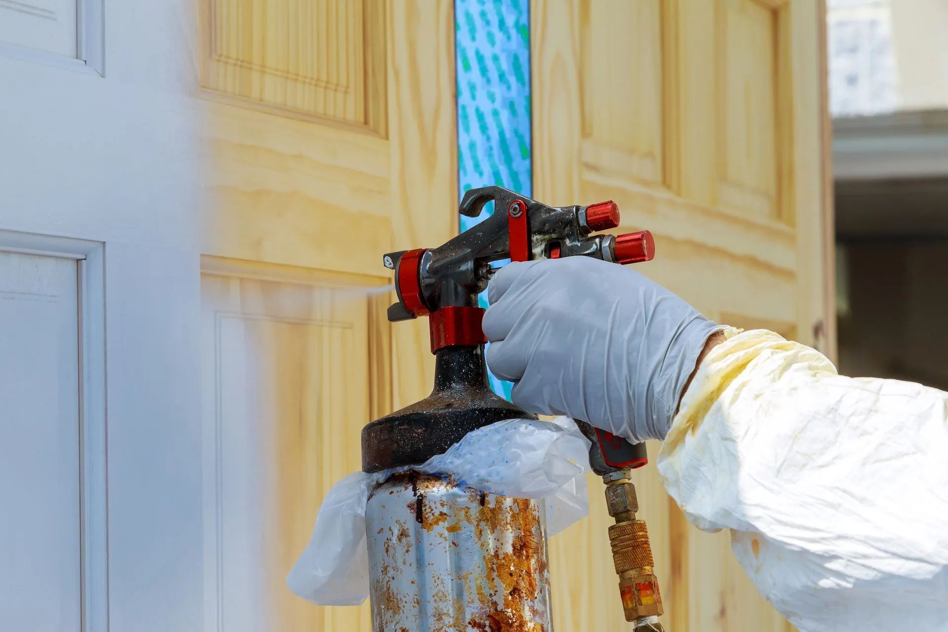 Person in protective gear spraying wood door with paint.