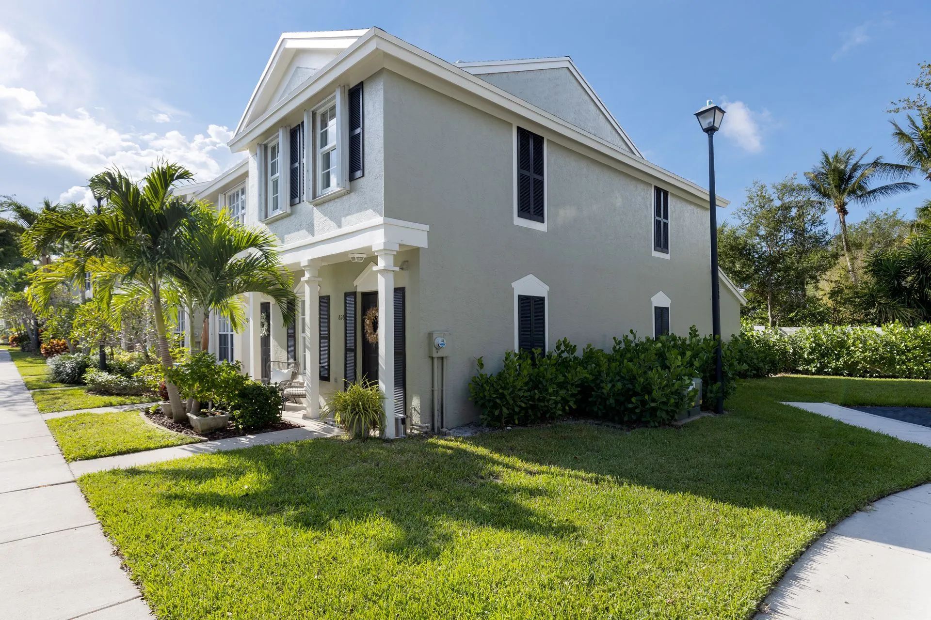 Two-story house with green lawn, sidewalk, and palm trees on a sunny day.