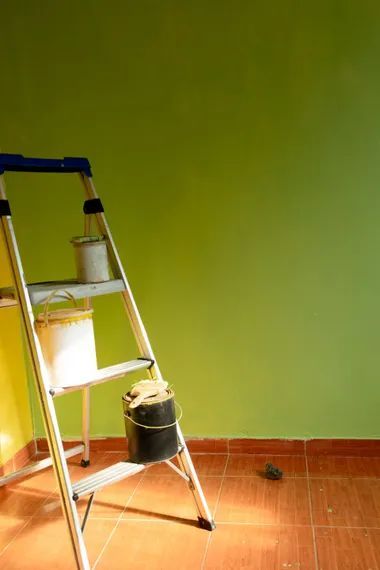 Ladder with paint cans against a green wall, setting up for painting.