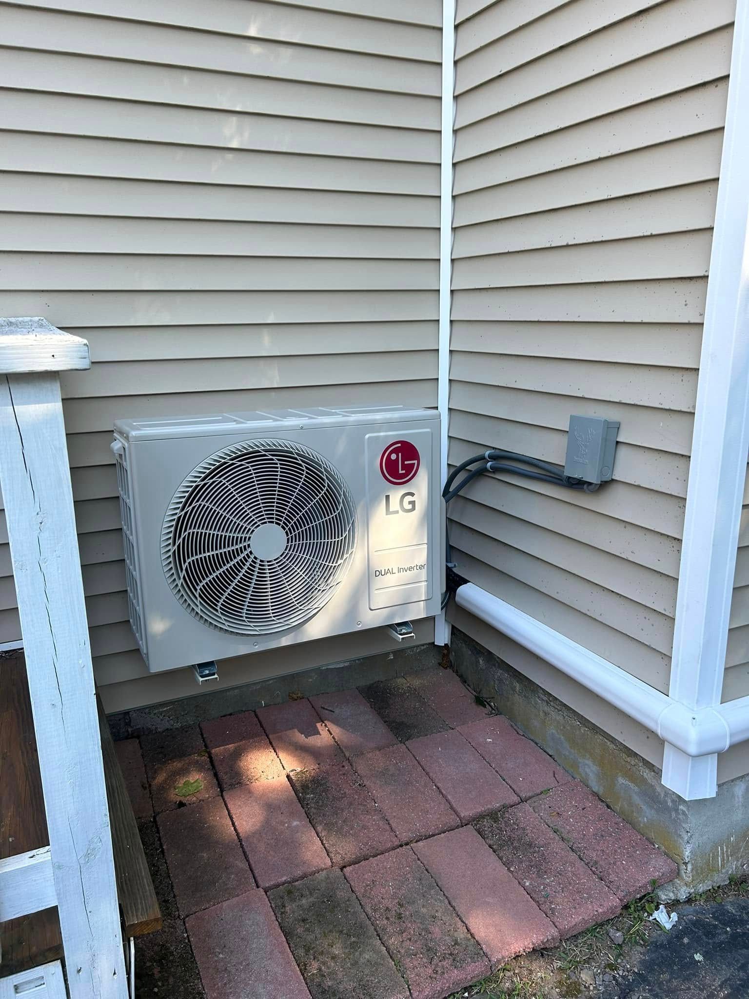 Two air conditioners are sitting next to each other on the side of a house.