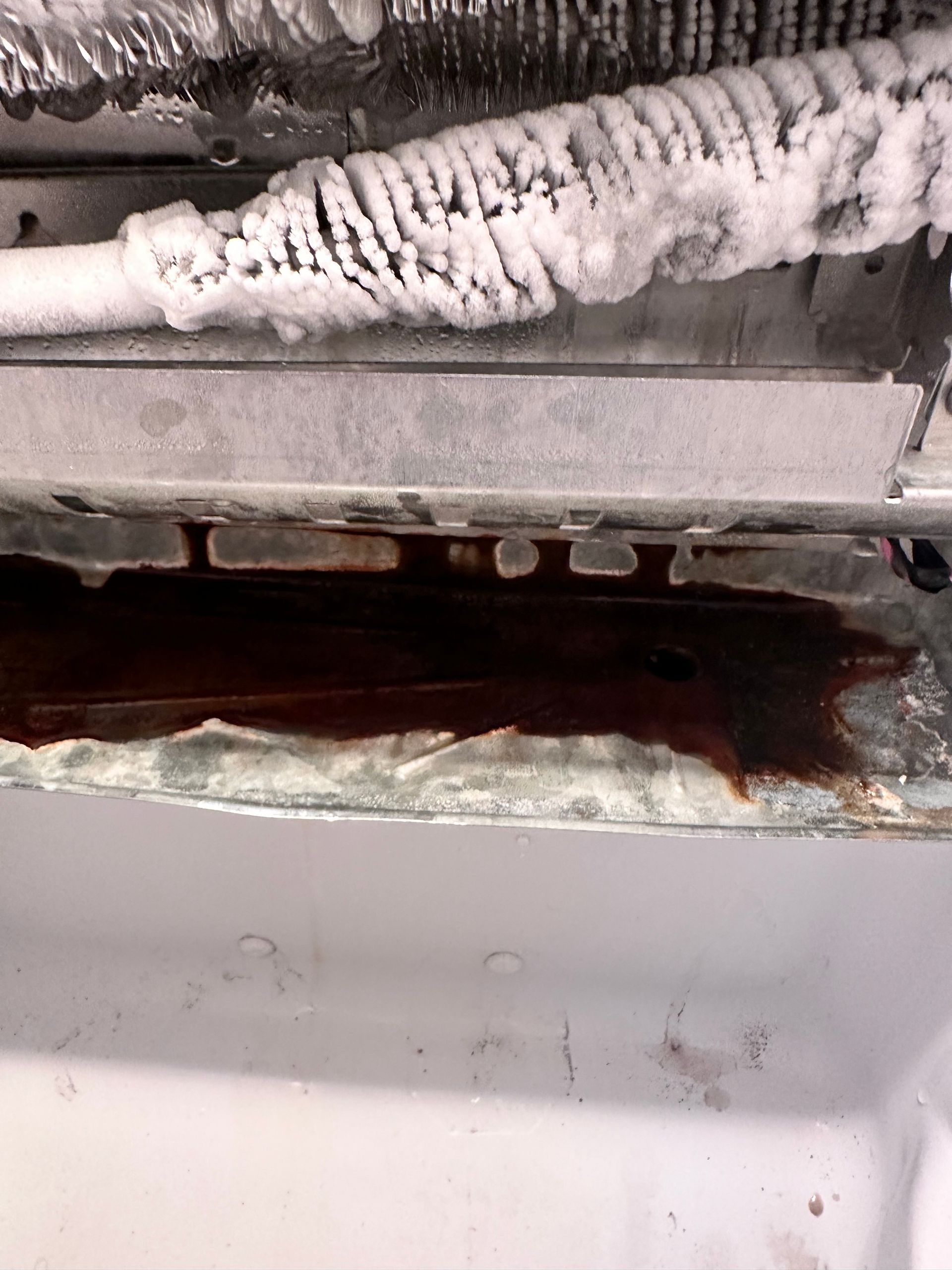 Inside of a refrigerator: ice buildup above a dark liquid pooling below.