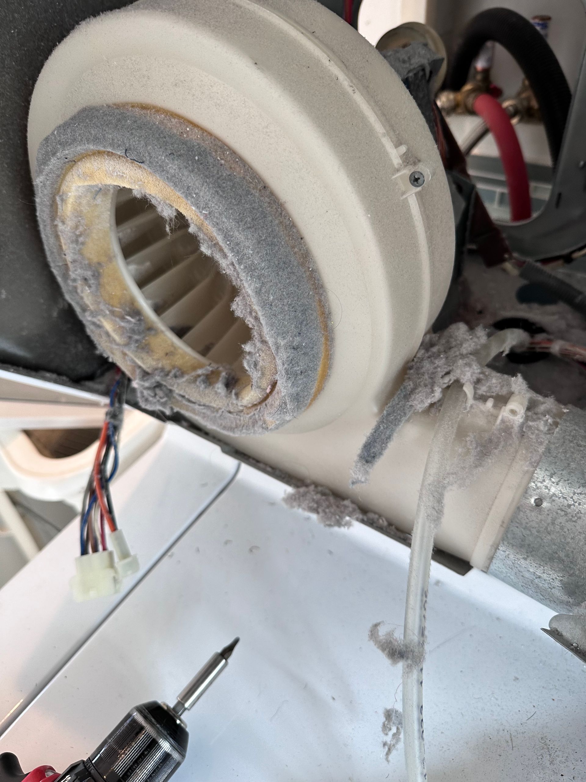 Close-up of a dusty blower fan inside a machine, possibly an HVAC unit, with wiring and a drill in the foreground.