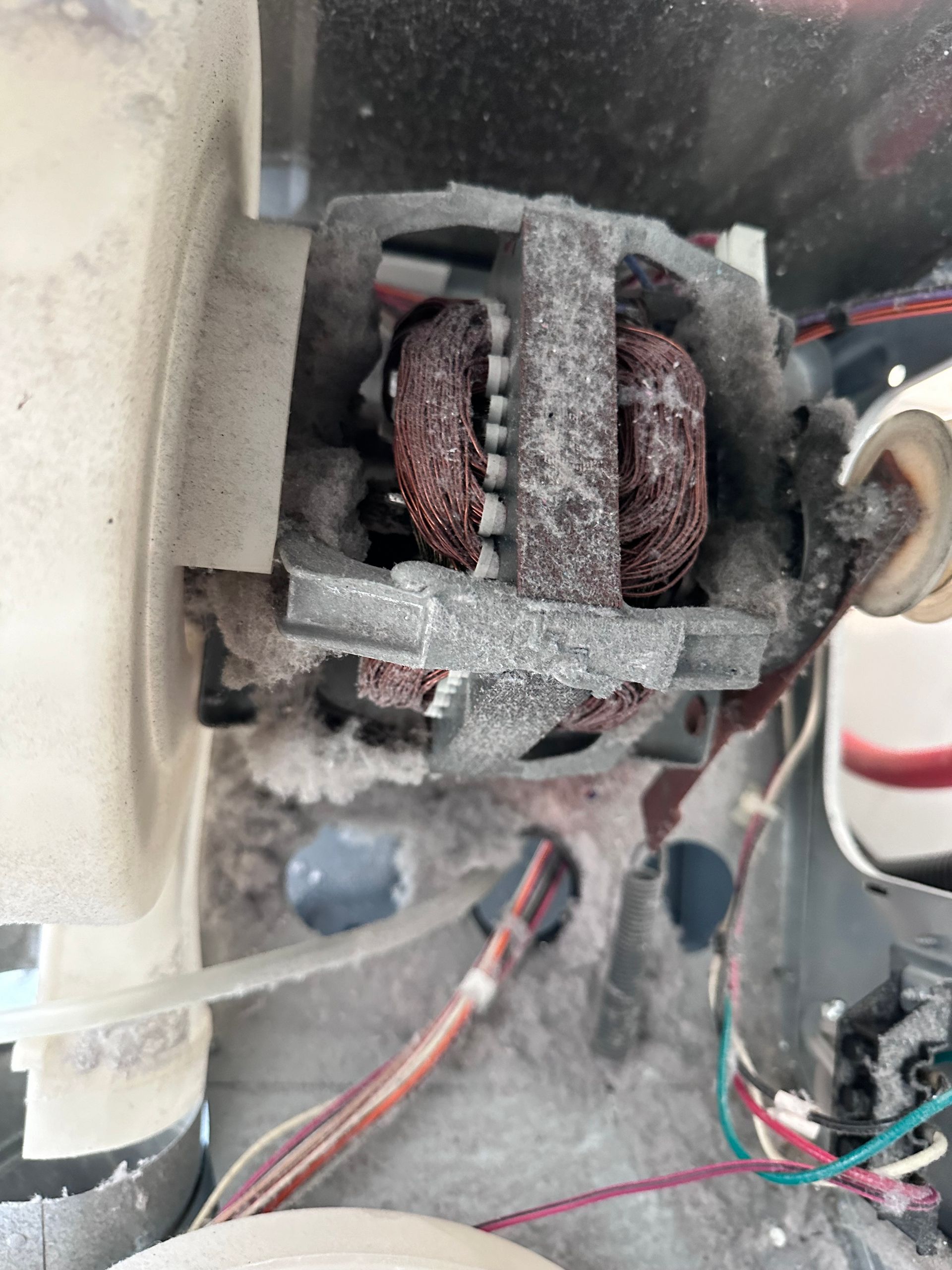 Close-up of a dryer motor heavily covered in lint and debris, with exposed copper wiring.